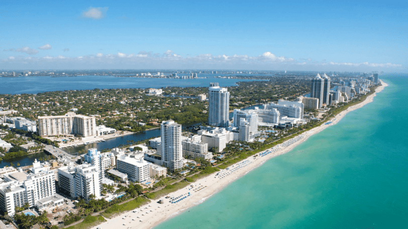 Aerial View Of A Sunny Day At Miami Beach, With Condos And Hotels Lined Up By The Beach