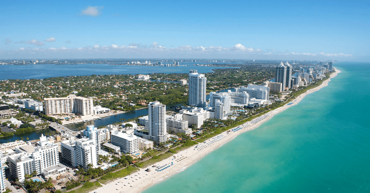 Aerial View Of A Sunny Day At Miami Beach, With Condos And Hotels Lined Up By The Beach