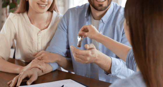 Close up image of a female realtor handling the keys to a new home owner couple