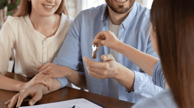 Close Up Image Of A Female Realtor Handling The Keys To A New Home Owner Couple