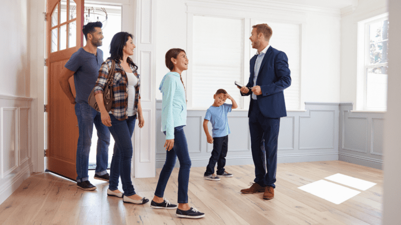 Male Realtor Showing The Interior Of A House To A Happy Hispanic Family