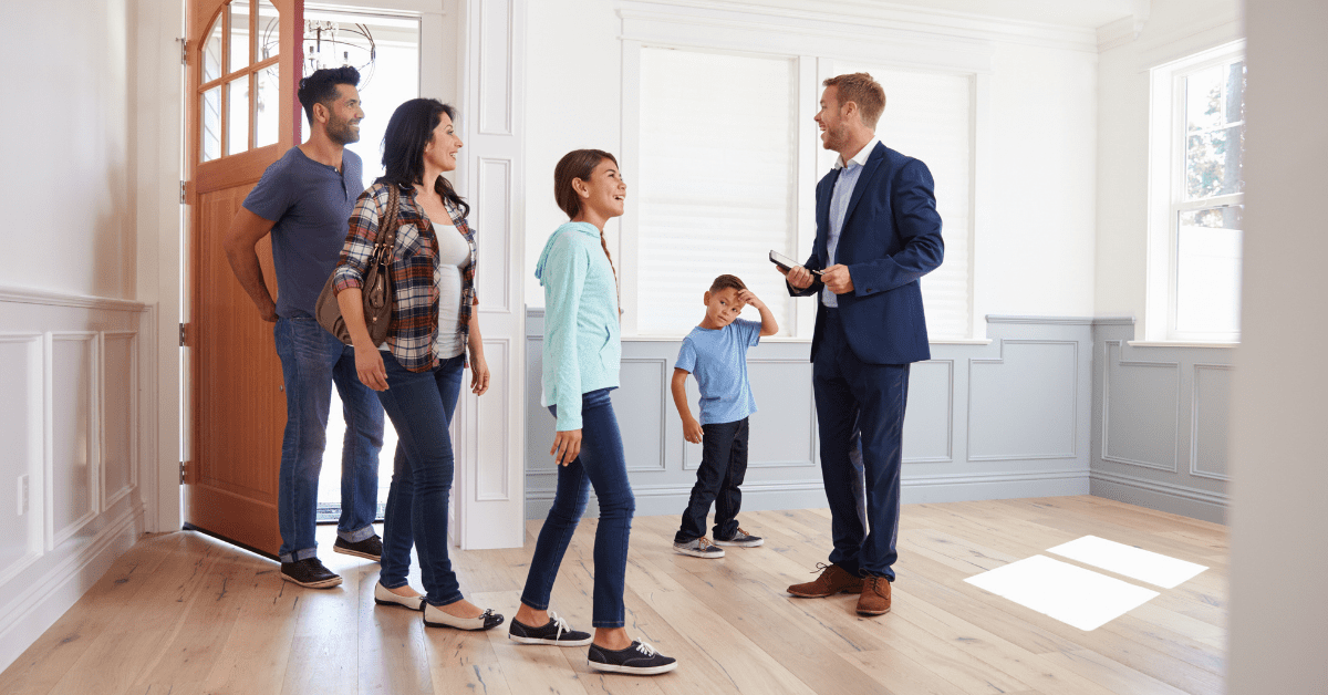 Male Realtor Showing The Interior Of A House To A Happy Hispanic Family
